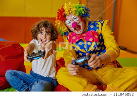 Portrait of little boy child and funny clown playing video games together Portrait of little boy child and funny clown playing video games together 111946098