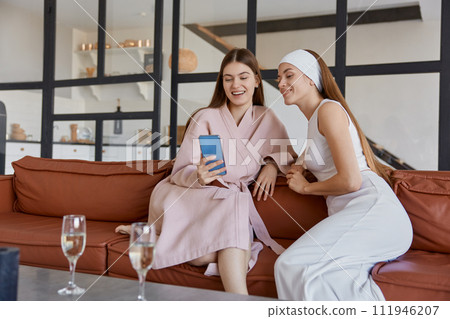 Young woman friends looking at smartphone screen sitting on sofa at home 111946207