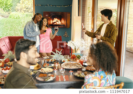 Cheerful man making photo on phone for smiling friends during festive home party 111947017
