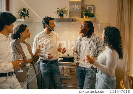 Group of smiling friends enjoying in conversation and drinking wine during Christmas party at home 111947018