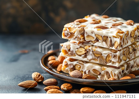 A stack of traditional Spanish dessert Turron with almonds on a ceramic plate on black background 111947131