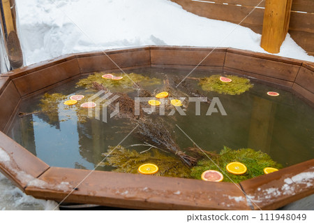 A hardwood bathtub filled with water and leaves sits amidst snow A hardwood bathtub filled with water and leaves sits amidst snow 111948049