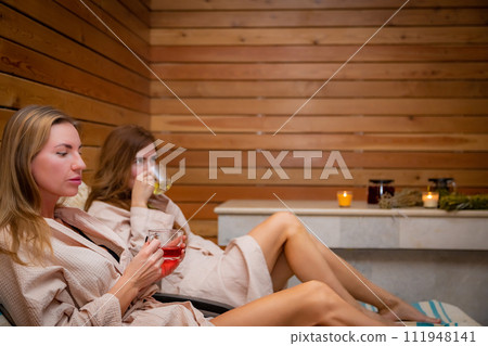 Two women enjoying wine in a sauna for comfort and relaxation Two women enjoying wine in a sauna for comfort and relaxation 111948141