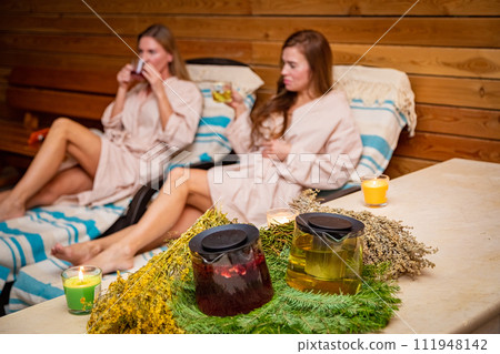 Happy women in sauna on sun loungers with herbal tea 111948142