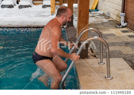 A man without a shirt is emerging from the water in a swimming pool A man without a shirt is emerging from the water in a swimming pool 111948189