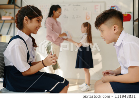 Smiling schoolgirl showing drawing in copybook to her classmate Smiling schoolgirl showing drawing in copybook to her classmate 111948831
