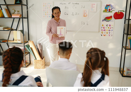 Cheerful teacher showing letters of English alphabet to school children Cheerful teacher showing letters of English alphabet to school children 111948837