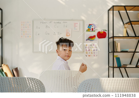 Portrait of schoolboy sitting on chair in front of whiteboard and looking back at camera 111948838