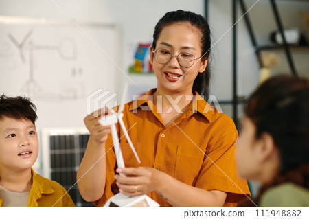 Cheerful teacher explaining schoolchildren wind turbine principle of work Cheerful teacher explaining schoolchildren wind turbine principle of work 111948882