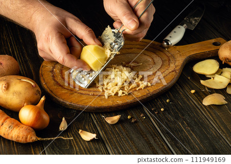 The chef grates potatoes to create a healthy dish for dinner or lunch. Idea of cooking fresh vegetables on kitchen table in hotel The chef grates potatoes to create a healthy dish for dinner or lunch. Idea of cooking fresh vegetables on kitchen table in hotel 111949169