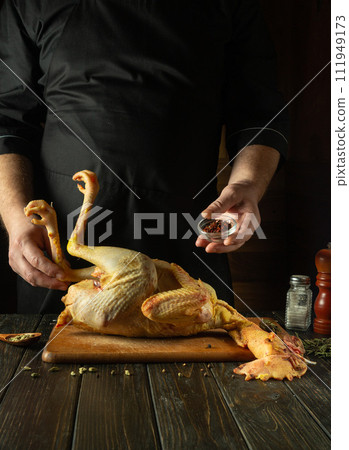 The cook preparing raw rooster in saloon kitchen. Before roasting, the cook adds spices to the rooster. Preparing to make an old-fashioned fried chicken recipe. The cook preparing raw rooster in saloon kitchen. Before roasting, the cook adds spices to the rooster. Preparing to make an old-fashioned fried chicken recipe. 111949173
