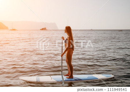 Woman sea sup. Close up portrait of happy young caucasian woman with long hair looking at camera and smiling. Cute woman portrait in a blue bikini posing on sup board in the sea Woman sea sup. Close up portrait of happy young caucasian woman with long hair looking at camera and smiling. Cute woman portrait in a blue bikini posing on sup board in the sea 111949541