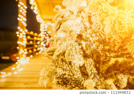 Snow-covered Christmas tree with bright white lights situated outdoors near a building, a welcoming festive moment. Snow-covered Christmas tree with bright white lights situated outdoors near a building, a welcoming festive moment. 111949651