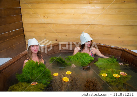 Two women bathing in a grassy landscape using a wooden tub Two women bathing in a grassy landscape using a wooden tub 111951231