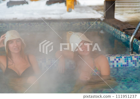 Two women in a swimming pool wearing bathing hats and relaxing in the hot tub 111951237