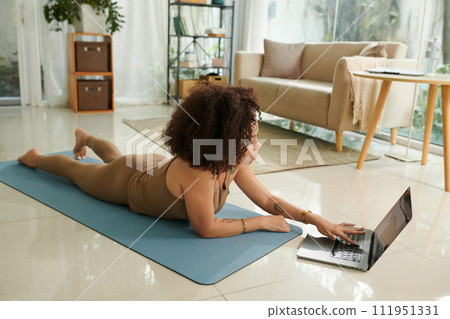 Woman following tutorial on laptop when working out at home Woman following tutorial on laptop when working out at home 111951331