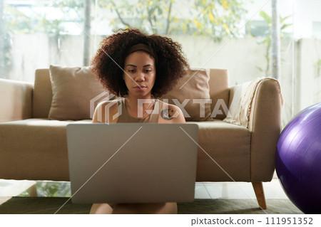 Serious Latin woman working in laptop in sunny living room Serious Latin woman working in laptop in sunny living room 111951352