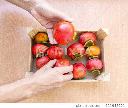 Close up man hands hold a wooden box with organic persimmons. 111952221