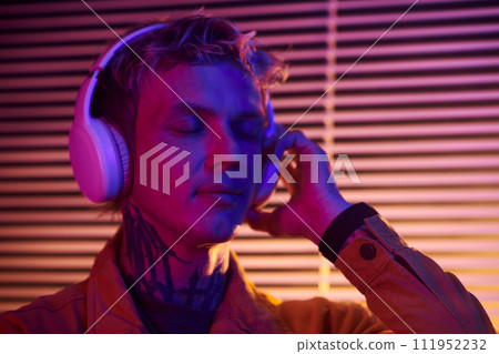 Portrait of young man closing eyes when listening to his favorite music track in headphones 111952232
