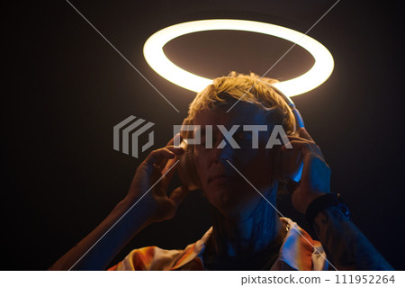 Portrait of dj standing under ring light and listening to music in headphones 111952264