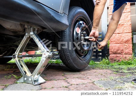 Person attempting to tighten nuts onto temporary car wheel after replacing the flat tire on the street Person attempting to tighten nuts onto temporary car wheel after replacing the flat tire on the street 111954252
