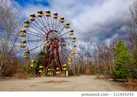 An idle Ferris wheel with yellow cars in a desolate area. 111954295