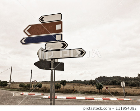 A signpost with five blank directional arrows at a road intersection, under a cloudy sky. 111954382