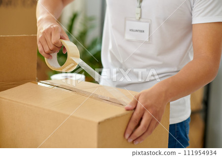 Cropped image of volunteer taping boxes in office of charity organization 111954934