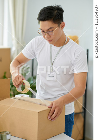 Volunteer taping box with packed goods for people in need Volunteer taping box with packed goods for people in need 111954937