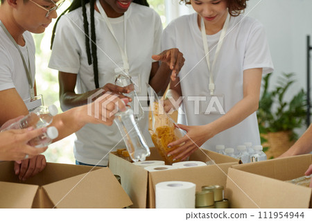 Charity organization workers putting packages of macaroni and bottled water in cardboard boxes Charity organization workers putting packages of macaroni and bottled water in cardboard boxes 111954944
