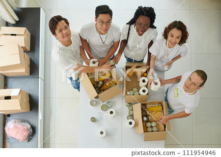 Group of cheerful volunteers packing products in boxes for refugees Group of cheerful volunteers packing products in boxes for refugees 111954946
