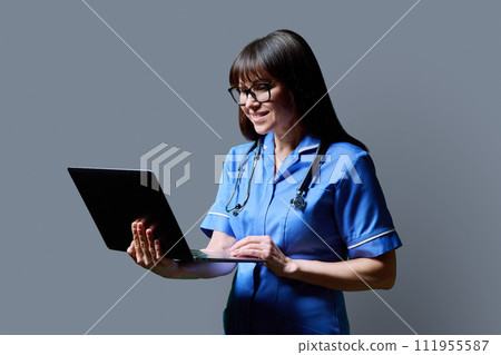 Female nurse using laptop, profile view on gray studio background 111955587