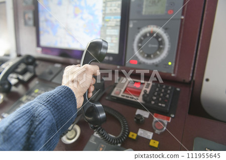 Navigational control panel and VHF radio with hand. Radio communication at sea. Working on the ship's bridge. 111955645
