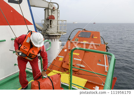 Seaman wearing lifejacket with vhf radio on Muster station. Abandon ship drill. Free fall boat. Cargo vessel. Seaman wearing lifejacket with vhf radio on Muster station. Abandon ship drill. Free fall boat. Cargo vessel. 111956170