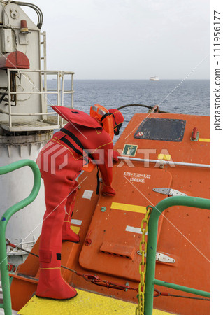 Seaman wearing Immersion Suit on Muster station. Abandon ship drill. Free fall boat. Cargo vessel. Seaman wearing Immersion Suit on Muster station. Abandon ship drill. Free fall boat. Cargo vessel. 111956177