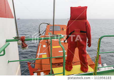 Seaman wearing Immersion Suit on Muster station. Abandon ship drill. Free fall boat. Cargo vessel. Seaman wearing Immersion Suit on Muster station. Abandon ship drill. Free fall boat. Cargo vessel. 111956183