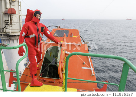 Seaman wearing Immersion Suit on Muster station. Abandon ship drill. Free fall boat. Cargo vessel. Seaman wearing Immersion Suit on Muster station. Abandon ship drill. Free fall boat. Cargo vessel. 111956187