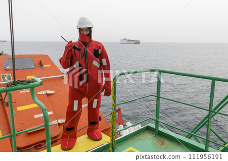 Seaman wearing Immersion Suit on Muster station. Abandon ship drill. Free fall boat. Cargo vessel. 111956191