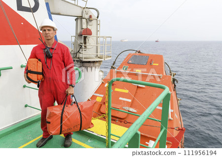 Seaman wearing lifejacket with vhf radio on Muster station. Abandon ship drill. Free fall boat. Cargo vessel. Seaman wearing lifejacket with vhf radio on Muster station. Abandon ship drill. Free fall boat. Cargo vessel. 111956194