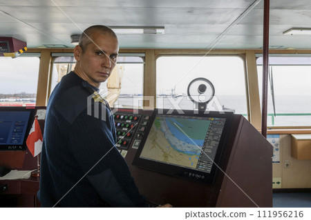 Officer on watch with electronic chart on the navigational bridge. Caucasian man in blue uniform sweater using ECDIS on the bridge of cargo ship. Officer on watch with electronic chart on the navigational bridge. Caucasian man in blue uniform sweater using ECDIS on the bridge of cargo ship. 111956216