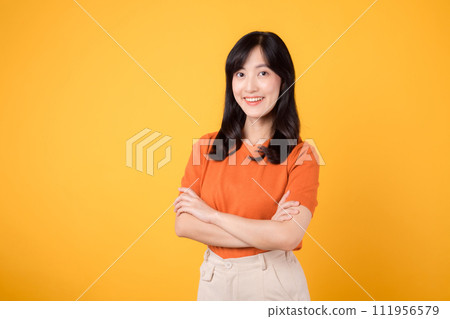 Embrace confidence with a young Asian woman in her 30s, donning an orange shirt, displaying crossed arm sign gesture on yellow background. Embrace confidence with a young Asian woman in her 30s, donning an orange shirt, displaying crossed arm sign gesture on yellow background. 111956579
