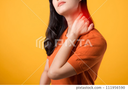 Aware Asian woman in her 30s, wearing an orange shirt, holds her pain neck on yellow background. office syndrome health care concept. Aware Asian woman in her 30s, wearing an orange shirt, holds her pain neck on yellow background. office syndrome health care concept. 111956590