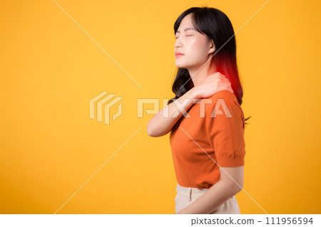 Aware young Asian woman in her 30s, wearing an orange shirt, holds her painful neck on yellow background. Neck ache therapy medical office syndrome concept. 111956594