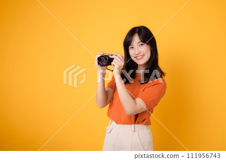 Stylish asian lady traveler with a camera isolated on yellow background, excited for an adventure-filled vacation. 111956743