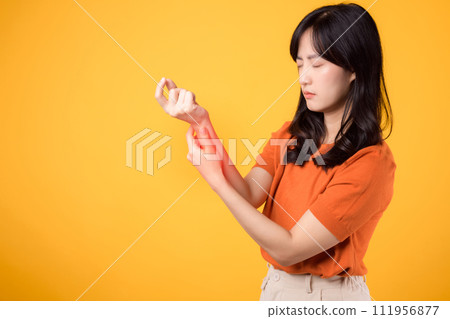 Woman wrist pain due to arthritis showcased in yellow studio portrait. Concept of injury and physical discomfort. 111956877