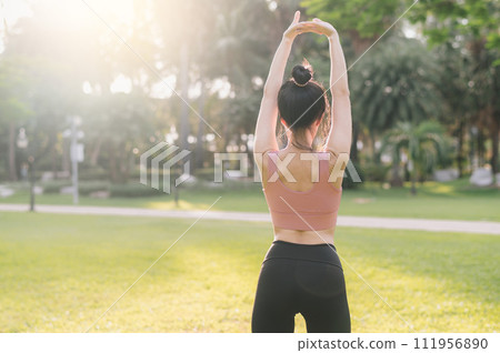 wellness and healthy lifestyle portrait 30s Asian woman in pink sportswear. preparing and stretching arm muscles before sunset run in the park. fitness outside and embrace balanced life. wellness and healthy lifestyle portrait 30s Asian woman in pink sportswear. preparing and stretching arm muscles before sunset run in the park. fitness outside and embrace balanced life. 111956890