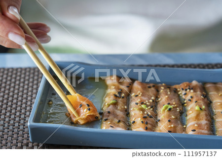 A woman with chopsticks in hand takes thin slices of salmon marinated 111957137
