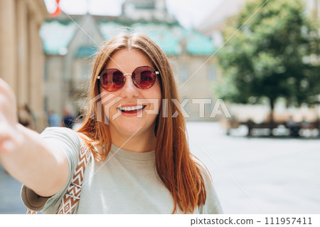 Photo relaxed charming positive young woman hold camera and make selfie summer outside in city center outdoors. Lifestyle tourist travel holiday concept. Point of view. Photo relaxed charming positive young woman hold camera and make selfie summer outside in city center outdoors. Lifestyle tourist travel holiday concept. Point of view. 111957411