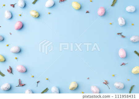 Festive Easter background. Multicoloured Easter eggs and flowers on a blue table. Card with a place for text. Top view. 111958431