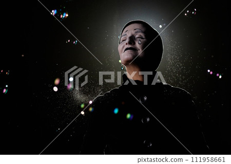 Minimal portrait of smiling mime artist playing with soap bubbles against black background, copy space 111958661